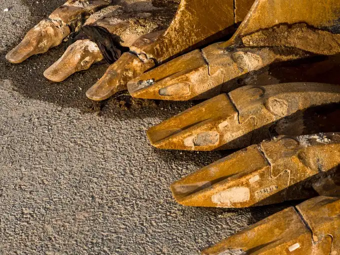 Row of worn yellow excavator bucket teeth resting on pavement