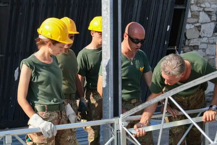 Crew in yellow hard hats, green T-shirts and camouflage trousers assembling a steel frame