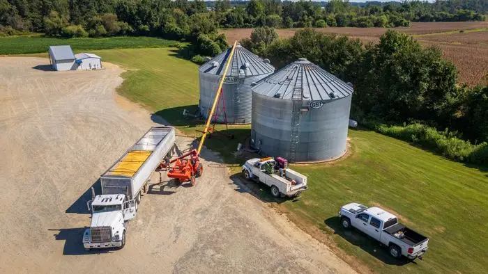 Aerial view of a grain truck loading at two steel silos on a farm