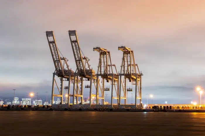 Row of ship-to-shore container cranes lit up at a port at dusk