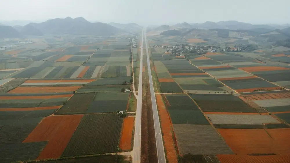 Aerial view of patchwork farm fields with a straight highway running toward distant hills