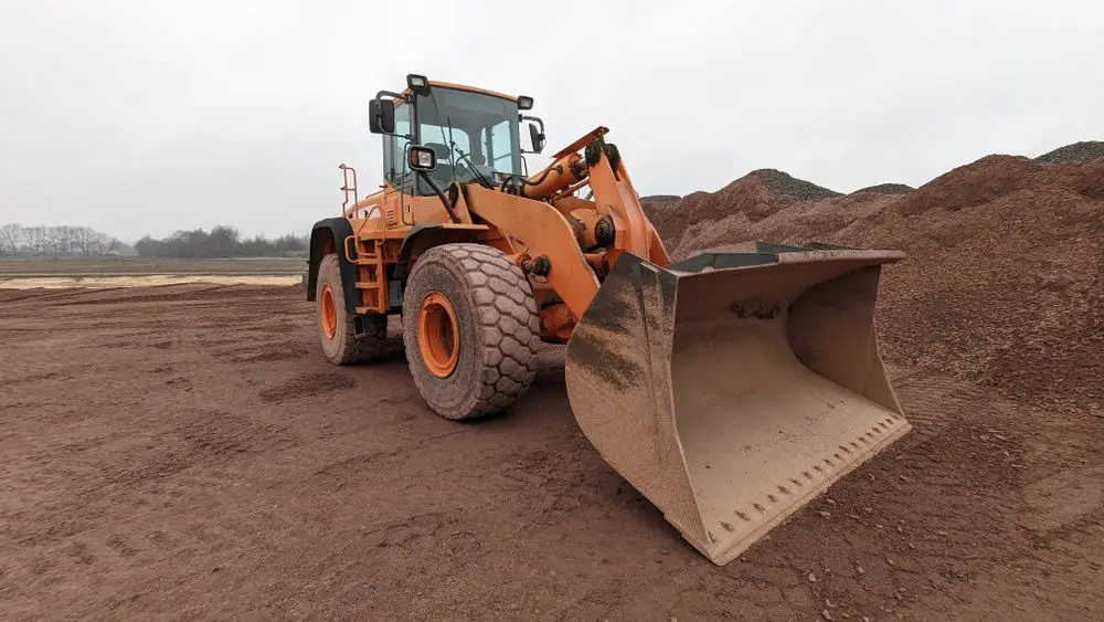 Orange wheel loader parked with its bucket down beside a red gravel stockpile